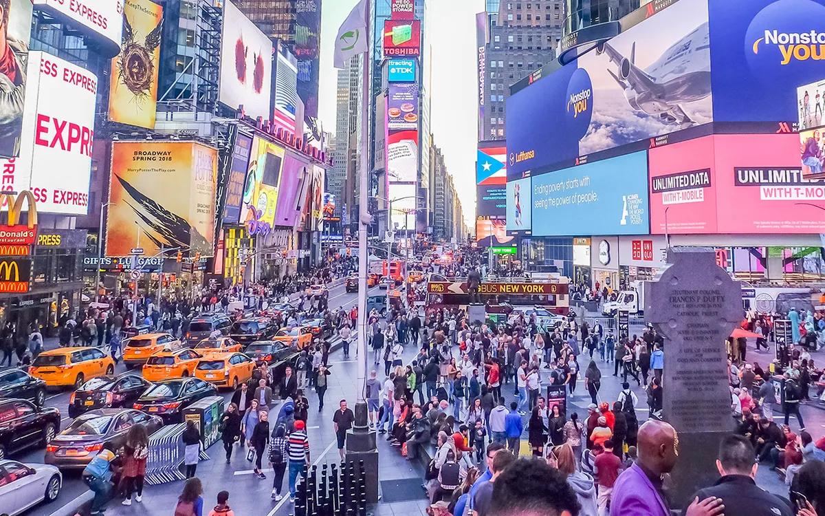 Times Square cheia de gente, táxis e painéis publicitários