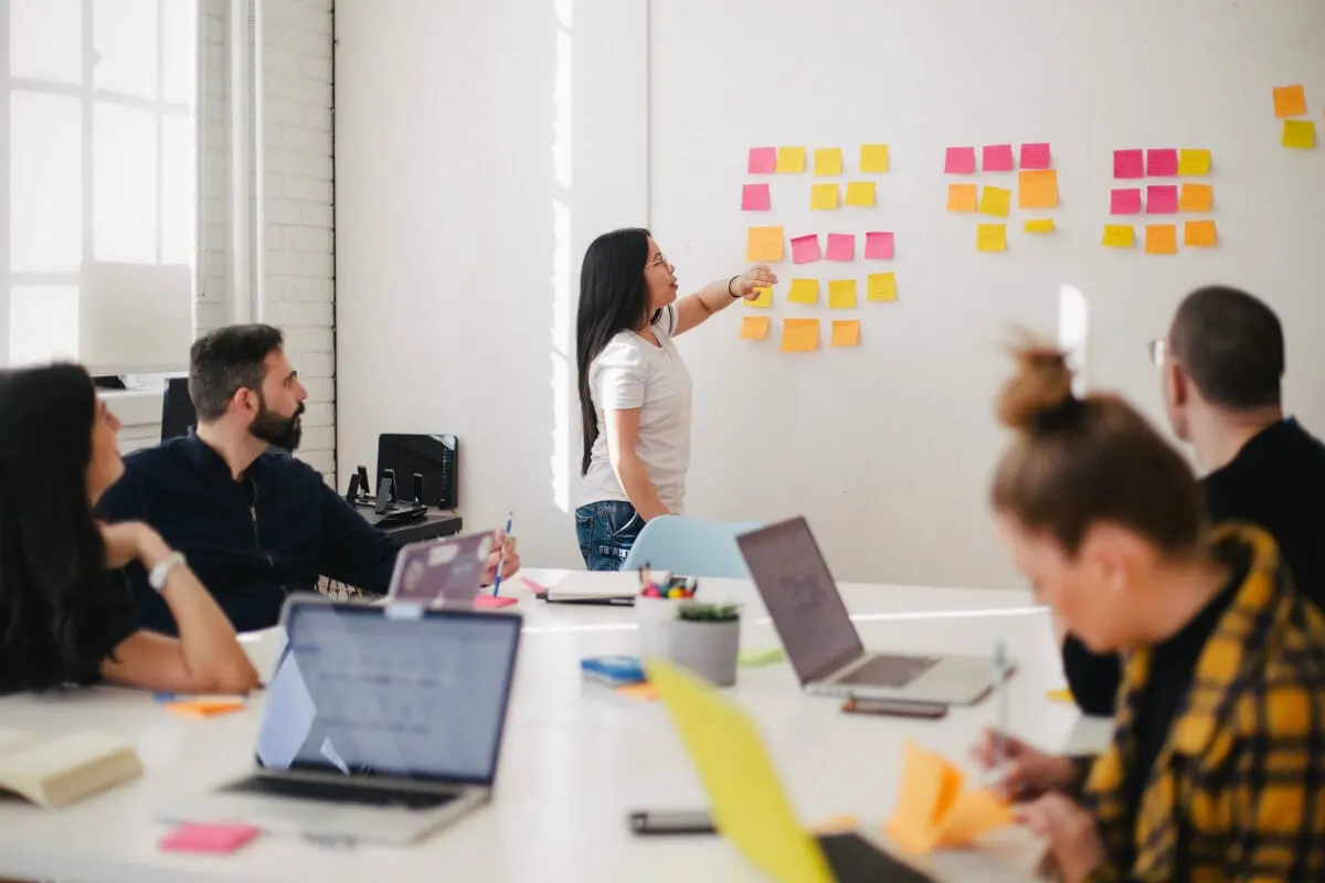 Facilitadora cola post-its em uma parede diante de colegas em uma reunião