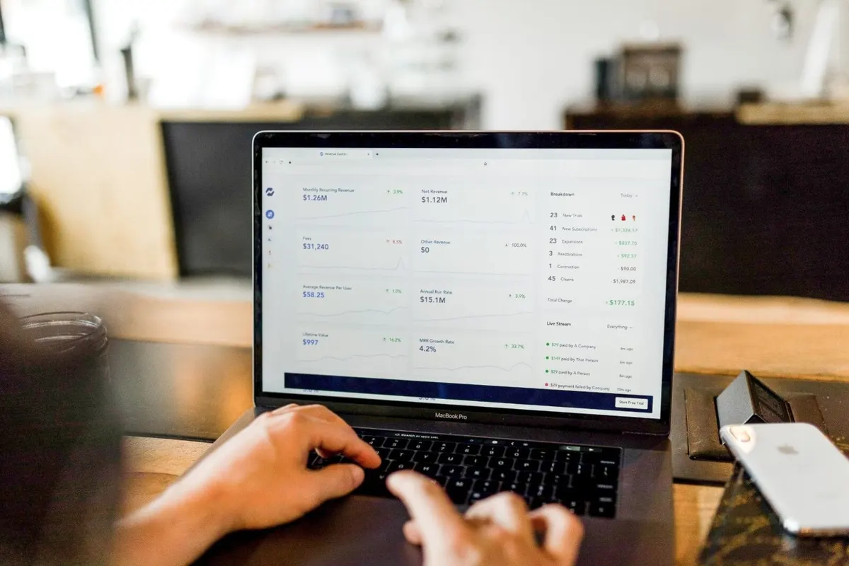 Mãos digitam em um notebook com um painel financeiro na tela