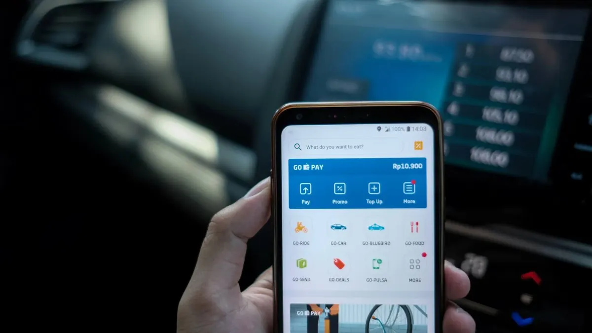 Mão segura um celular com um aplicativo de pagamentos, dentro de um carro