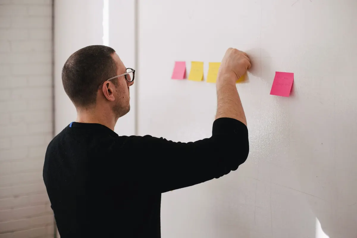 Homem de óculos cola post-its coloridos em uma parede branca