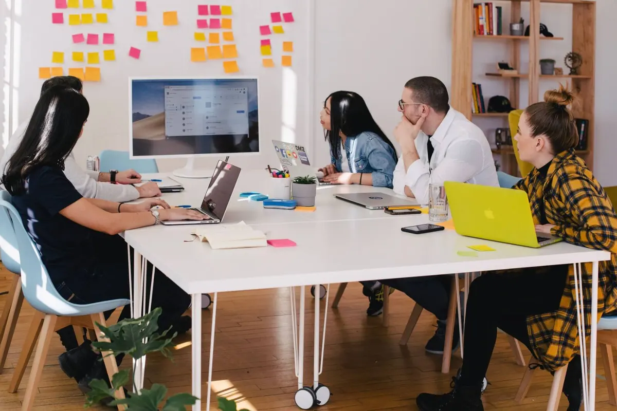 Grupo de pessoas em uma reunião em volta de uma mesa branca, com post-its na parede
