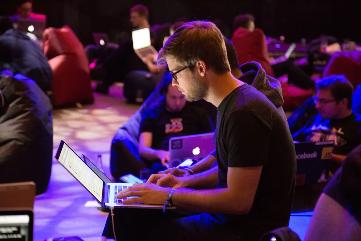 Pessoas trabalham em notebooks em um evento com iluminação roxa