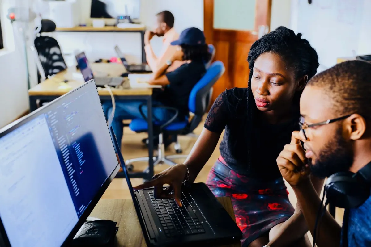 Duas pessoas trabalham juntas diante de um notebook, em um escritório