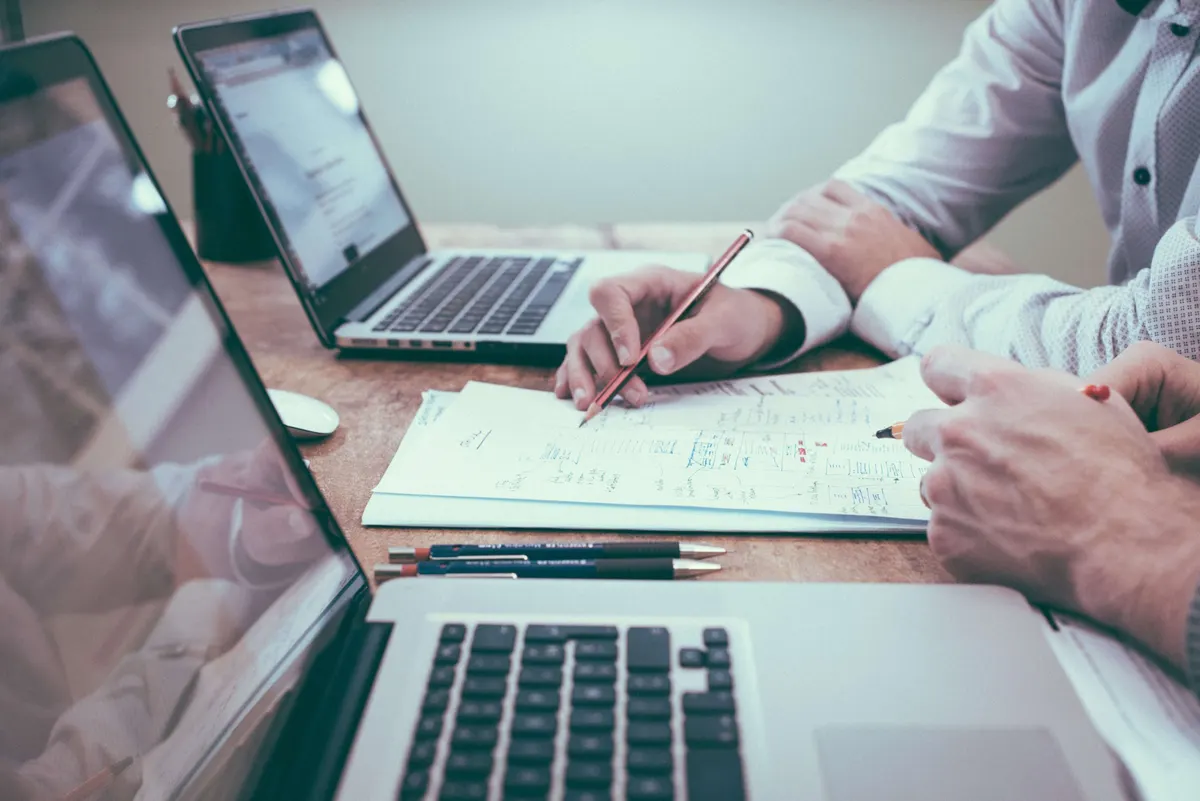 Duas pessoas trabalham com notebooks e anotações sobre uma mesa