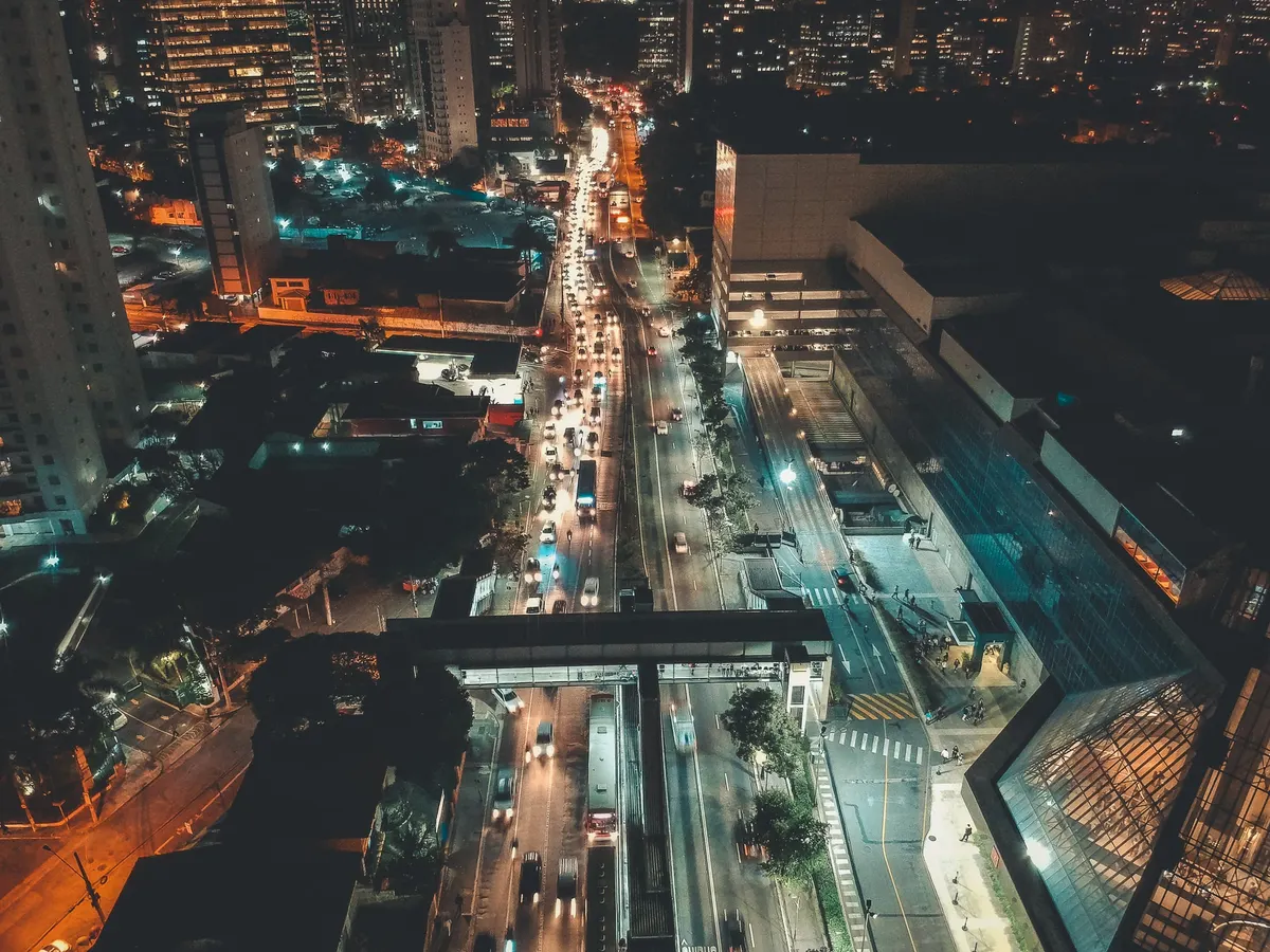 Vista noturna de uma avenida movimentada, com prédios iluminados